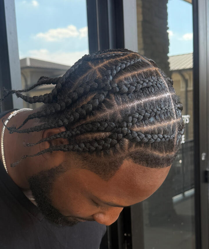 A close-up of a man with a fresh haircut and groomed beard, wearing a barber cape inside a modern barbershop.